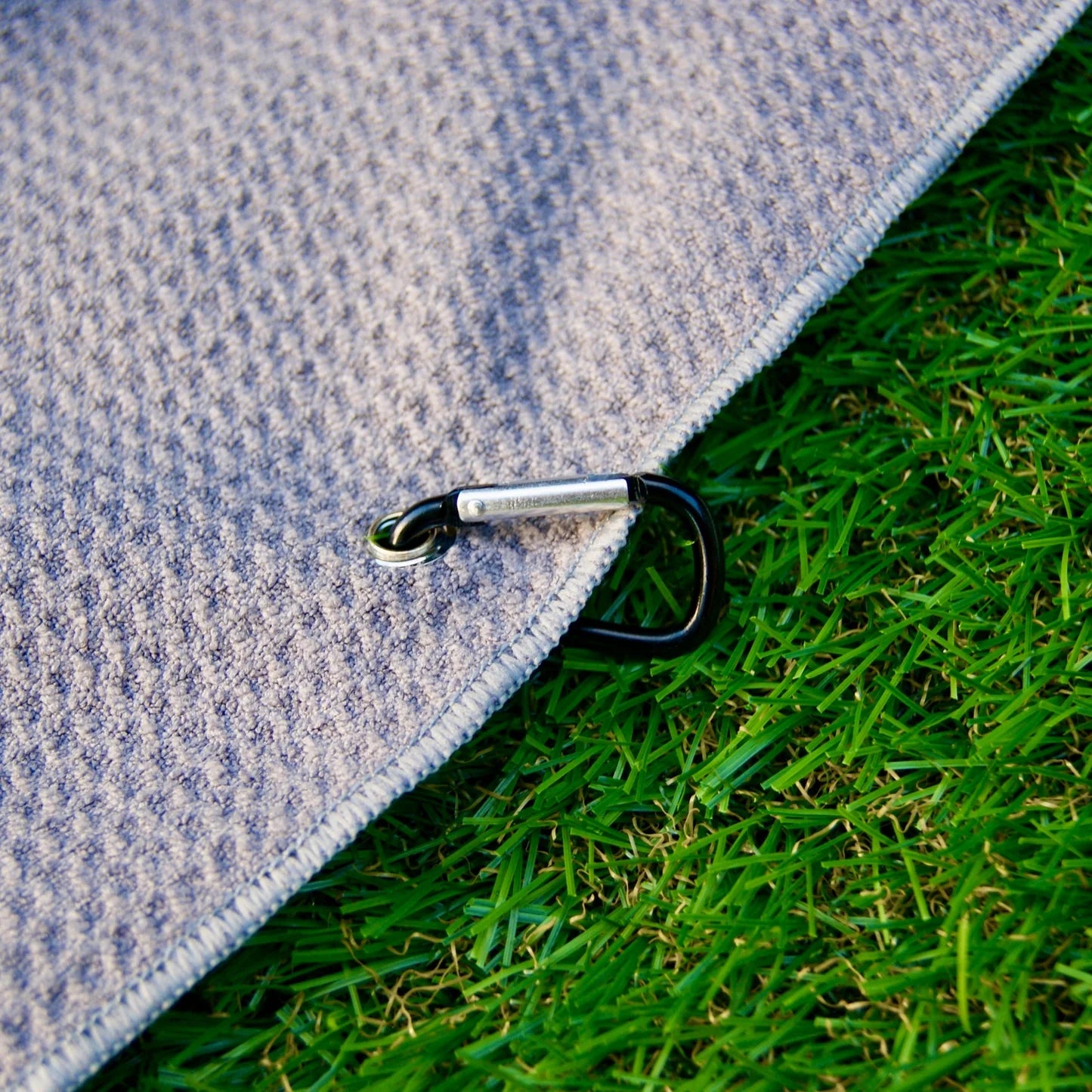 Bamboo tri-fold golf towel with carabiner clip on grass, eco-friendly golf club cleaner, sustainable microfiber towel for golfers.